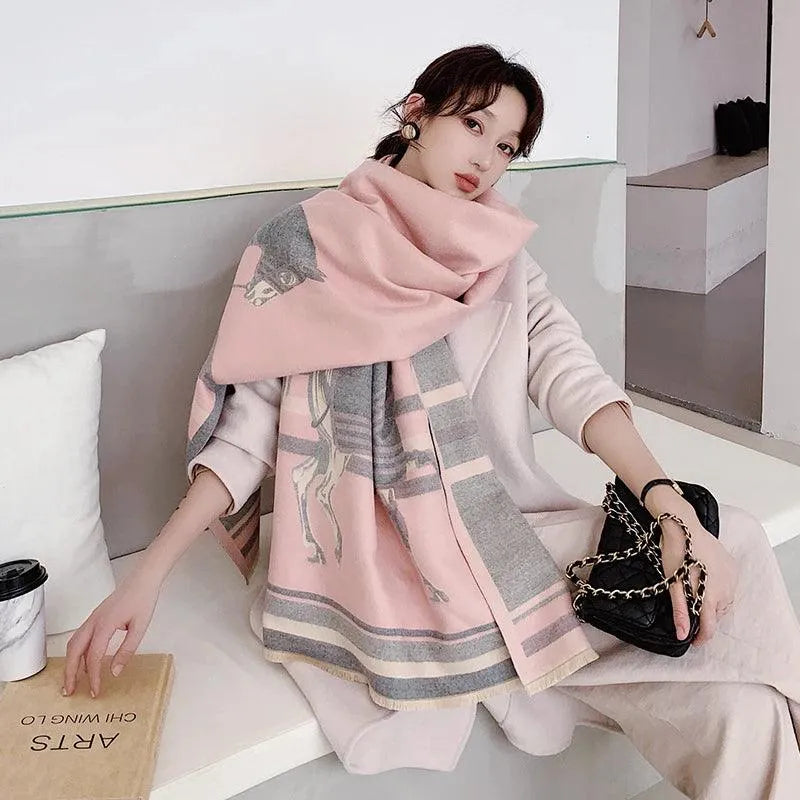 A person wearing a pastel pink cashmerette scarf with an equestrian print, draped over the shoulders, seated in a cozy indoor setting.