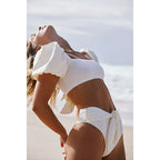 Woman wearing a white bikini with ruffled details on a beach.