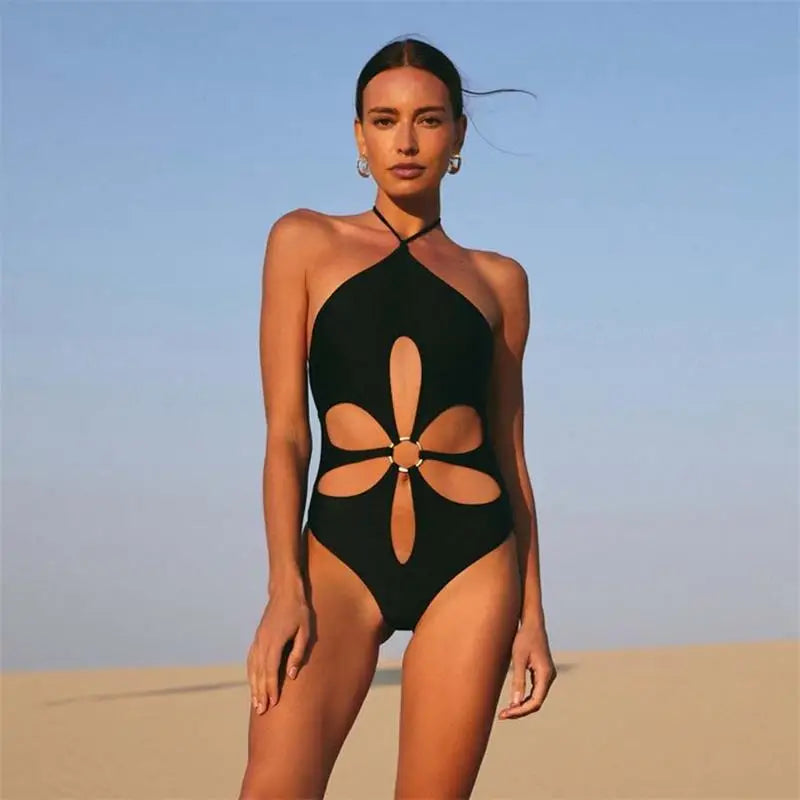 Woman wearing a black halter neck swimsuit with floral cutouts on a beach.