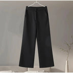 Black pants hanging on a hanger against a neutral background.