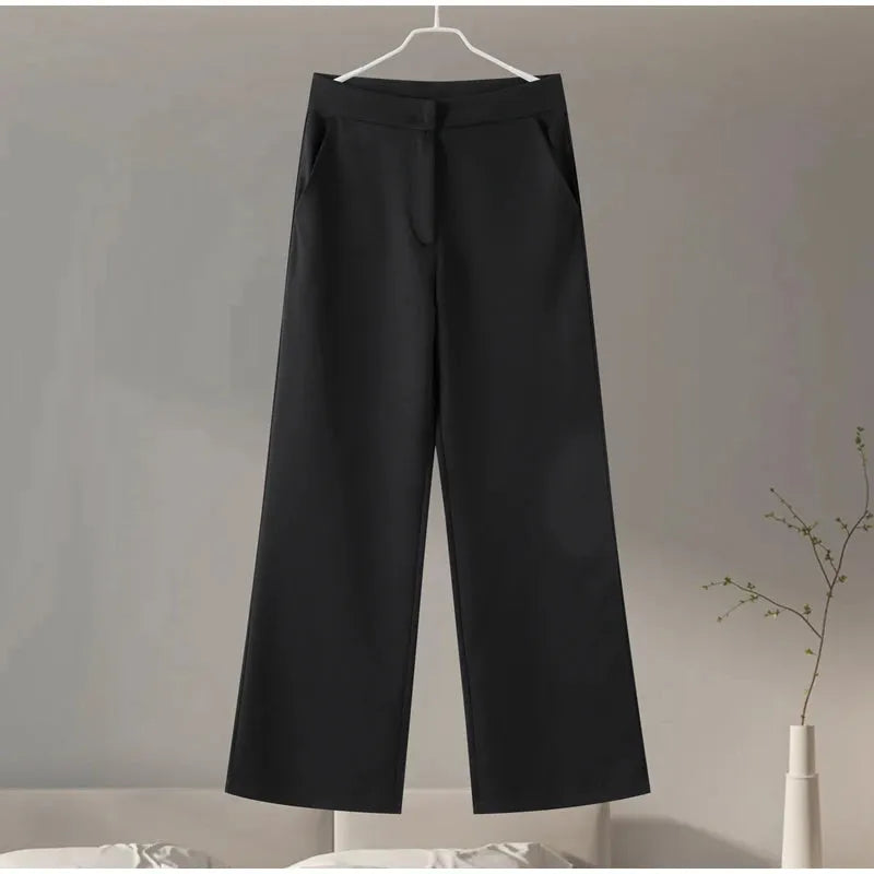 Black pants hanging on a hanger against a neutral background.