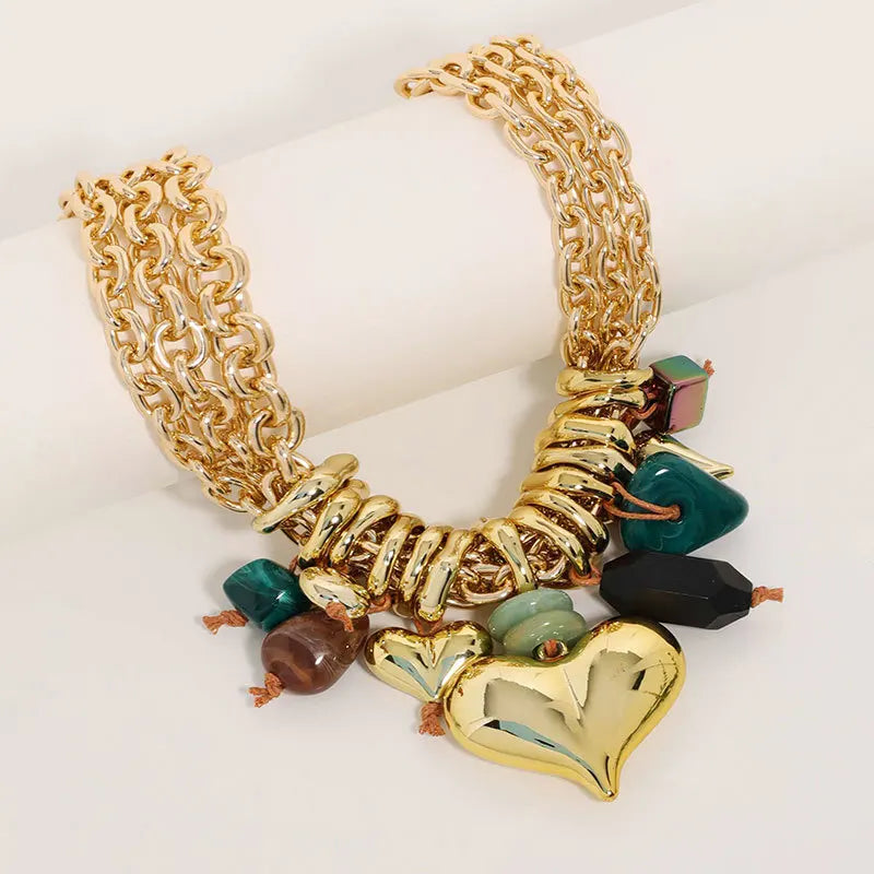 Gold chain bracelet with heart and bead charms on a white background