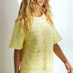 A woman wearing a pale yellow short-sleeve crochet knit cardigan with a button front and textured openwork pattern, shown against a bright white background.