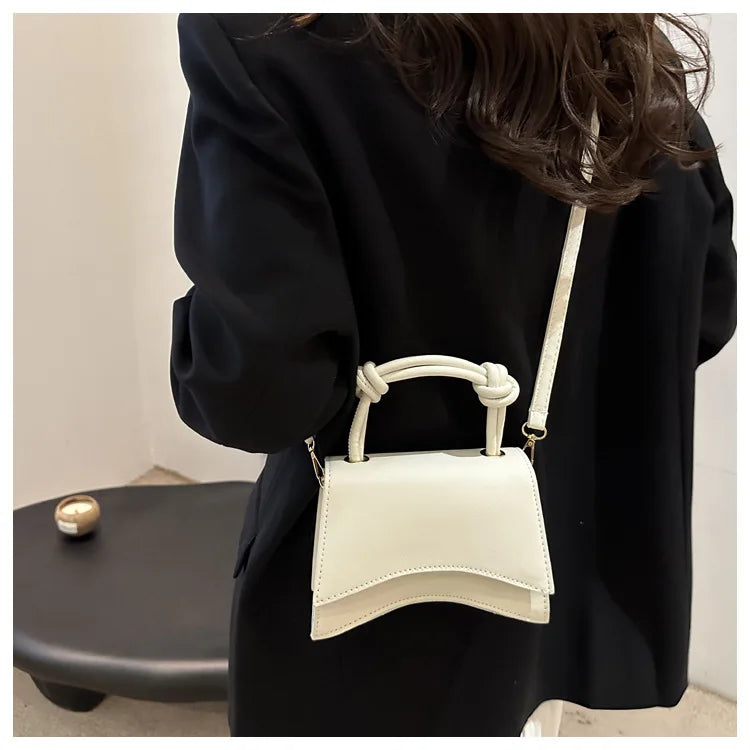 Person wearing a black outfit with a white handbag on a neutral background