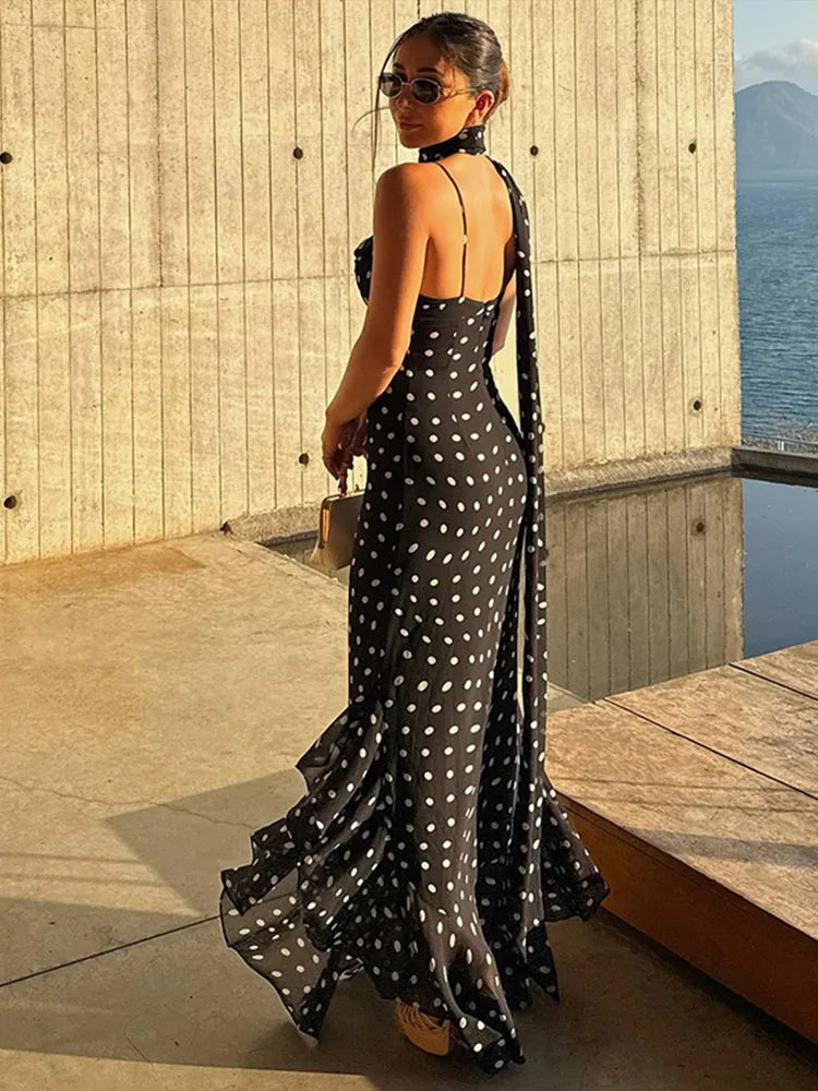 Woman in a black polka dot dress standing by a wooden platform with water and mountains in the background.