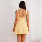 A rear view of a woman wearing a yellow sleeveless square neck mini dress with lace-up details at the front.