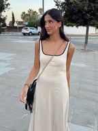Woman in a white dress standing on a sidewalk with trees and cars in the background