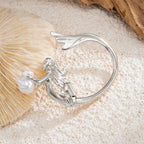 Silver ring with a pearl on a sandy surface with a shell in the background