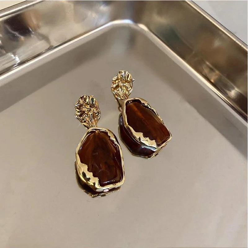 Gold and brown earrings on a reflective surface