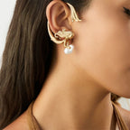 Gold earring with a pearl on a model's ear against a neutral background