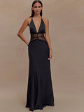 Woman wearing a black evening gown with a deep neckline and embellished belt on a beige background