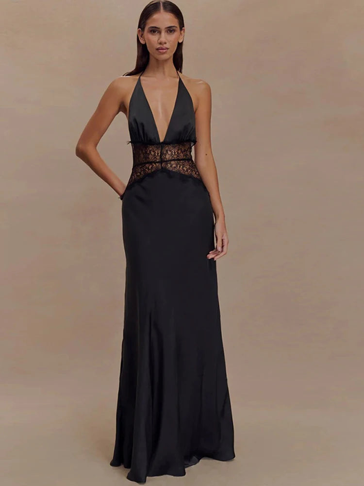 Woman wearing a black evening gown with a deep neckline and embellished belt on a beige background