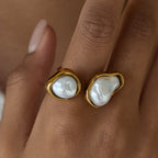 Gold rings with pearl-like stones on a hand against a neutral background