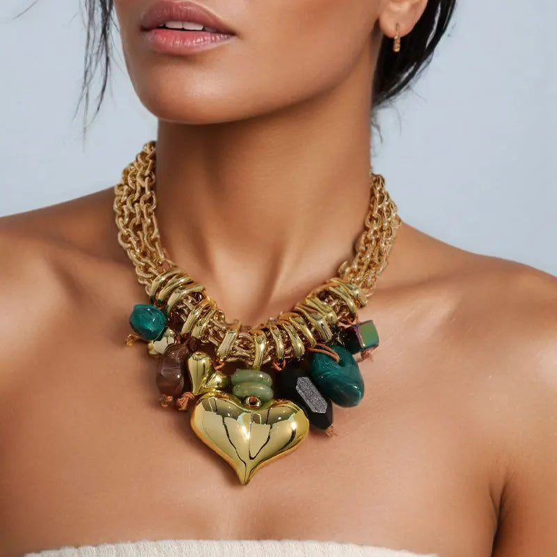 Gold necklace with heart pendant and colorful stones worn by a model against a light blue background