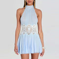 A woman wearing a light blue halter mini dress with a pleated skirt and a white lace embroidered waistband, shown against a plain light gray studio background.