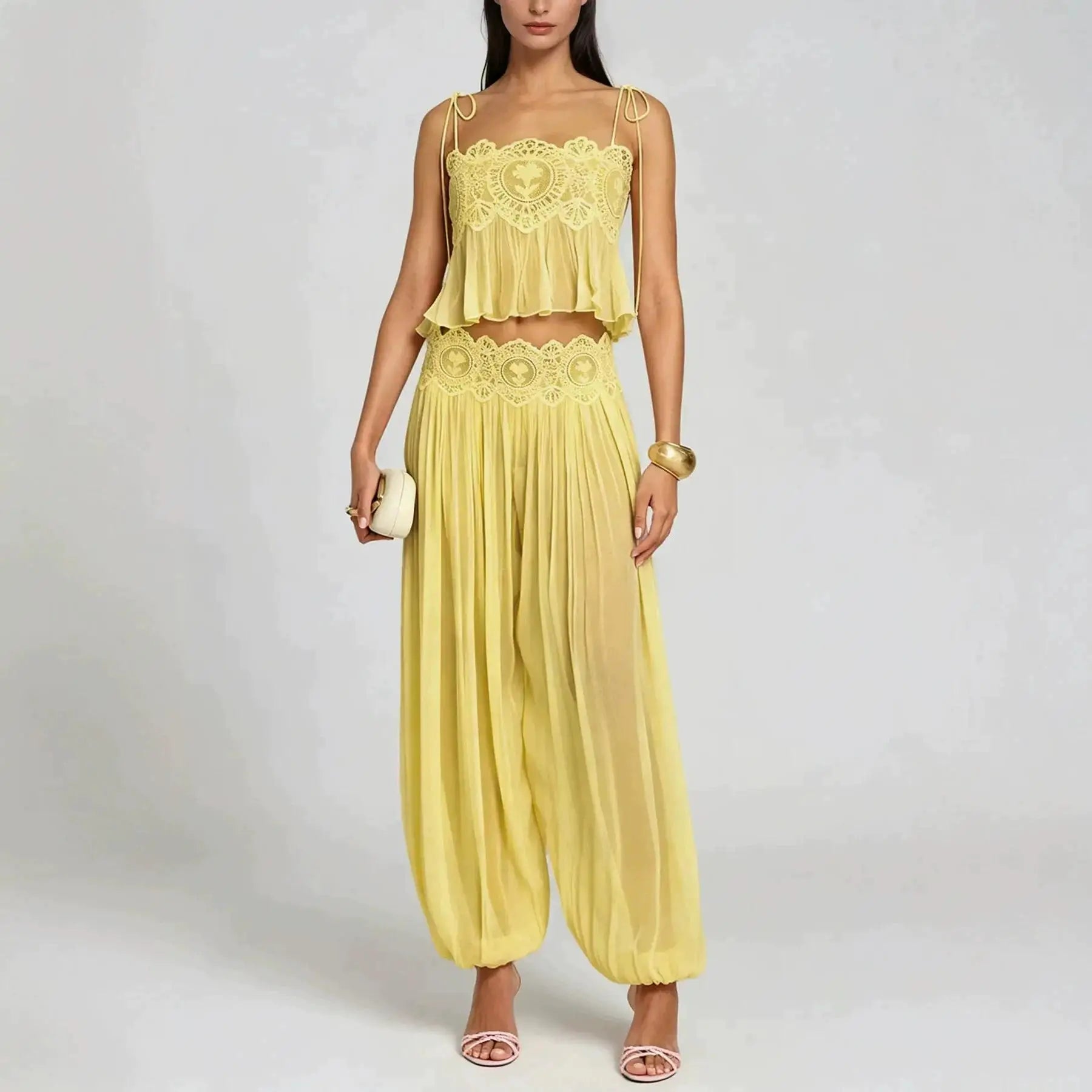 A woman models a two-piece yellow two-tone set featuring a ruffled crop top with lace detailing and matching pleated harem pants, set against a plain light gray background.