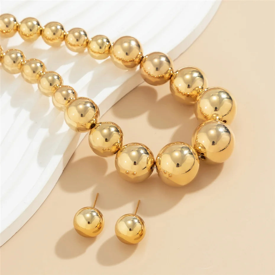 Gold beaded bracelet and earrings on a beige surface
