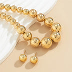 Gold beaded bracelet and earrings on a beige surface
