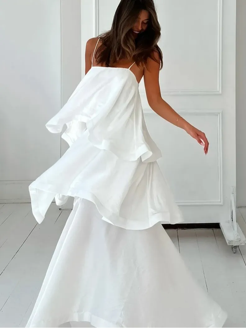 A woman wearing a white pleated maxi dress with a square neckline and spaghetti straps.