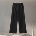 Black pants hanging on a hanger against a neutral background.