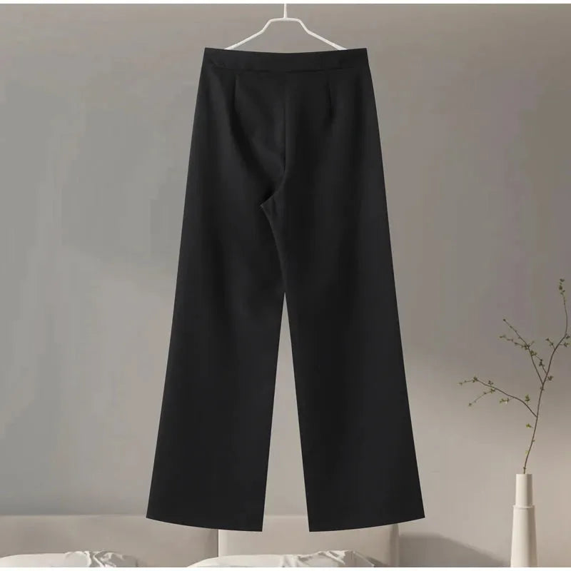Black pants hanging on a hanger against a neutral background.