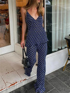 A woman wearing a navy two-piece outfit with a geometric pattern, consisting of a sleeveless top with a V-neck and wide-leg pants, standing in front of a glass door.