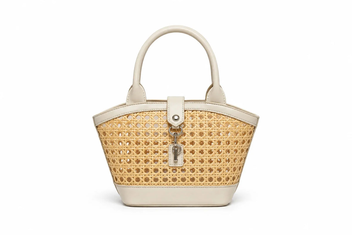 A structured handbag with a woven natural cane body and cream-colored faux leather trim, featuring dual top handles and a front turn-lock clasp with a hanging key charm, shown on a plain white background.