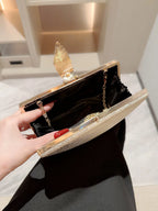 Gold clutch with feather design held by a hand against a neutral background
