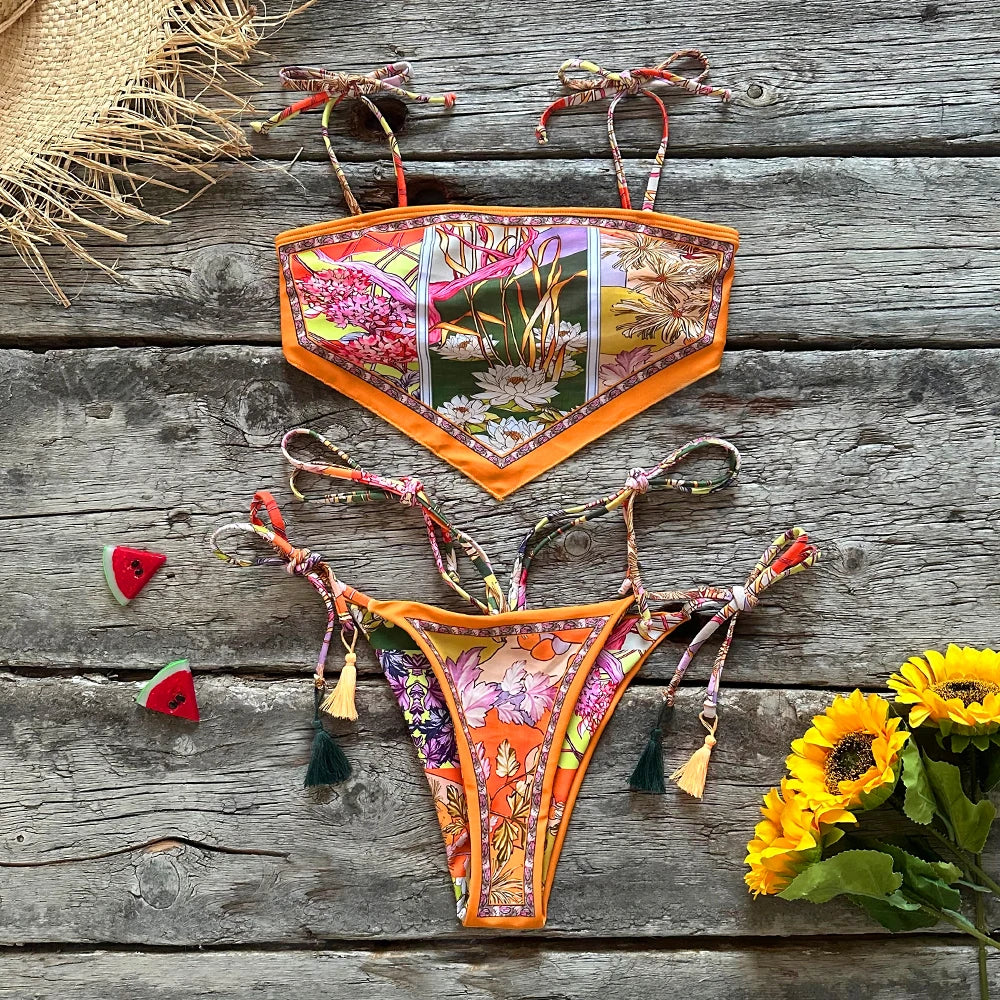 Colorful bikini set on a wooden surface with flowers and a straw hat.