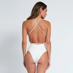 Woman wearing a white swimsuit with thin straps on a light gray background