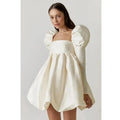 Woman wearing a white dress with puff sleeves against a plain background