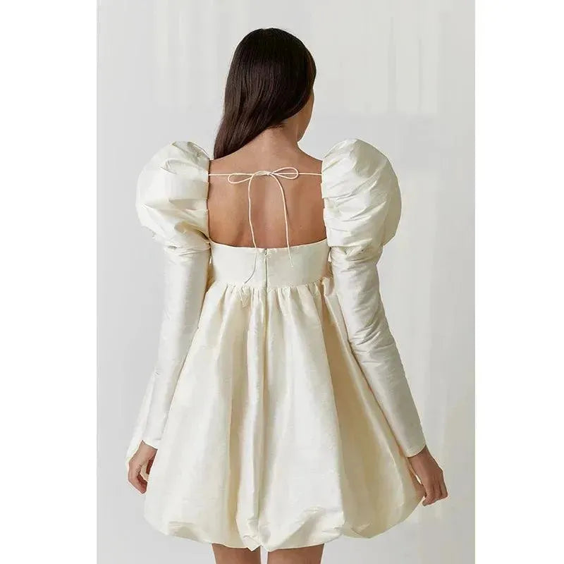 Woman wearing a cream-colored dress with puff sleeves and a bow at the back.