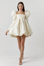 Woman wearing a white dress with puffed sleeves on a plain background