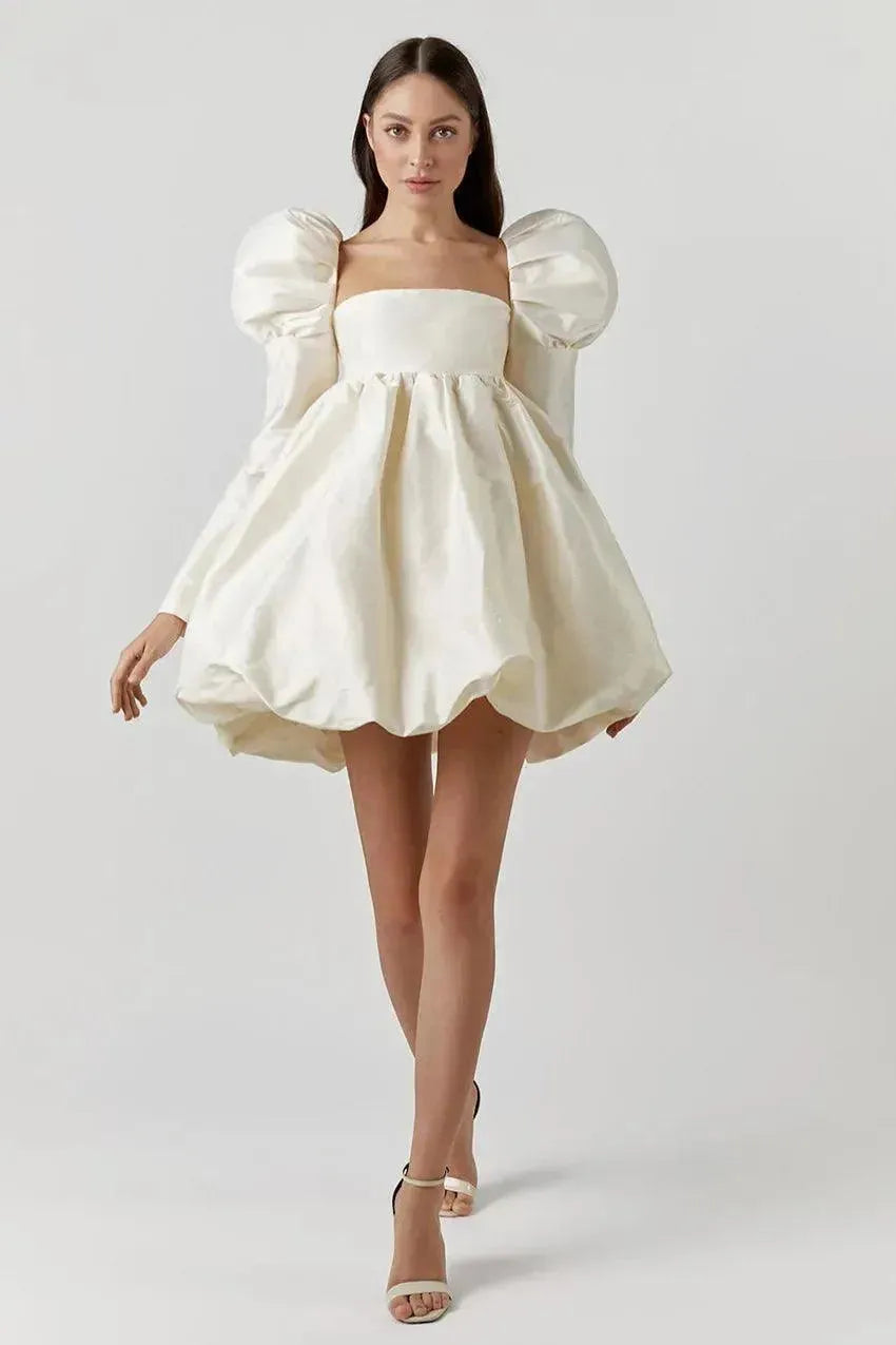 Woman wearing a white dress with puffed sleeves on a plain background
