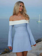 Woman in light blue off-shoulder dress standing by the sea.