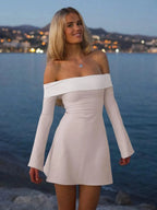 Woman in white off-shoulder dress by the sea at night.