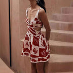 A woman wearing a red and white floral mini dress with a V-neck and sleeveless design, standing on a staircase.
