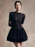 Woman wearing a black dress with a textured pattern on a neutral background.