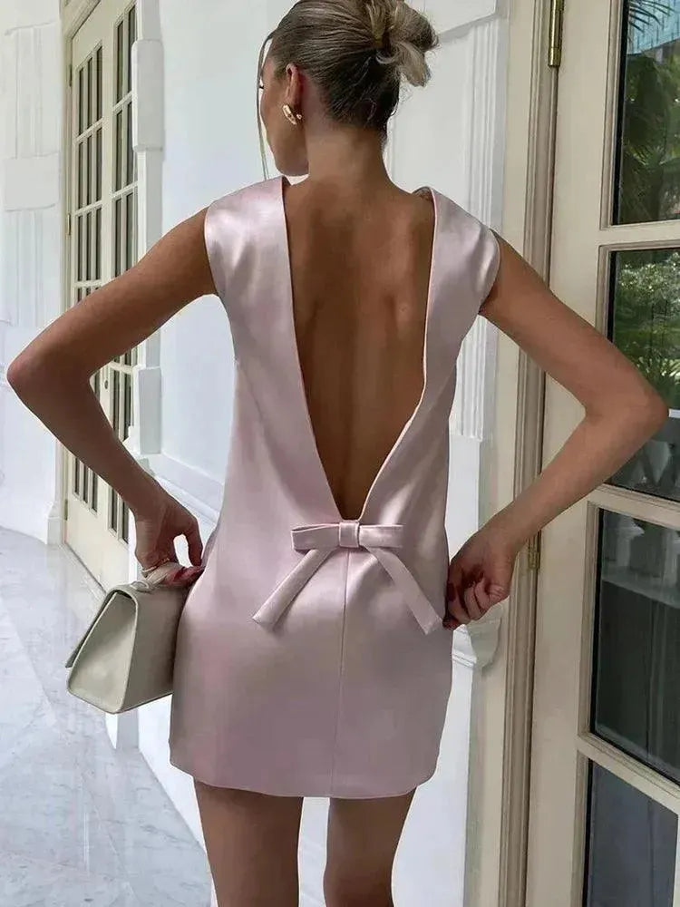 Woman in a light pink dress with a bow, standing in a doorway.