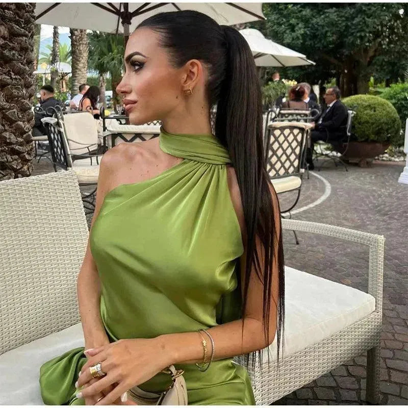 Woman in a green dress sitting outdoors with palm trees in the background.