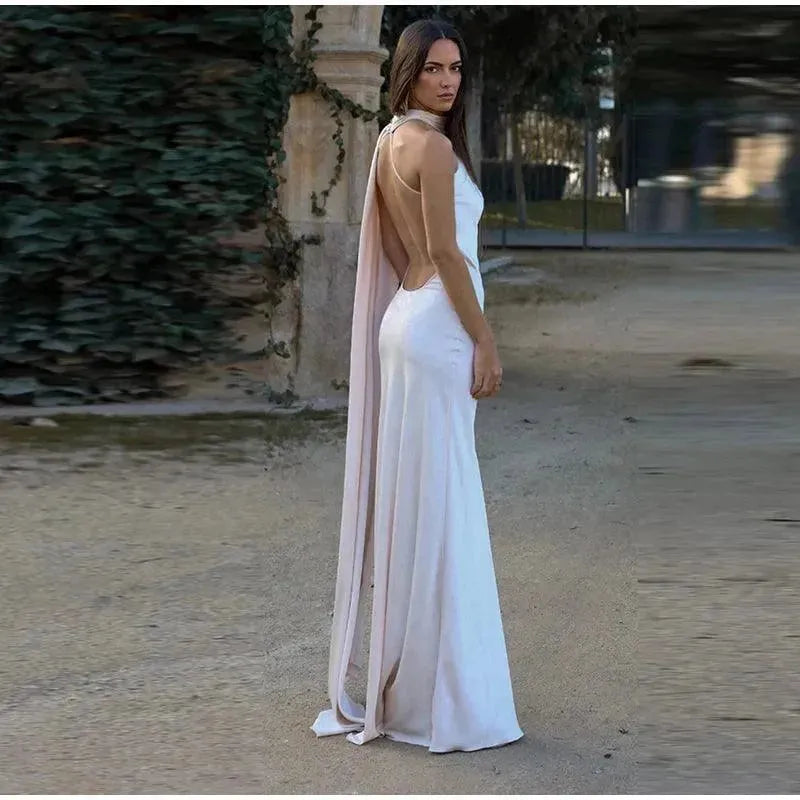 Woman in a white gown with a cape-like feature standing in a garden setting.