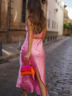 A woman wearing a pink, sleeveless, A-line mid-calf satin dress and carrying a red handbag.