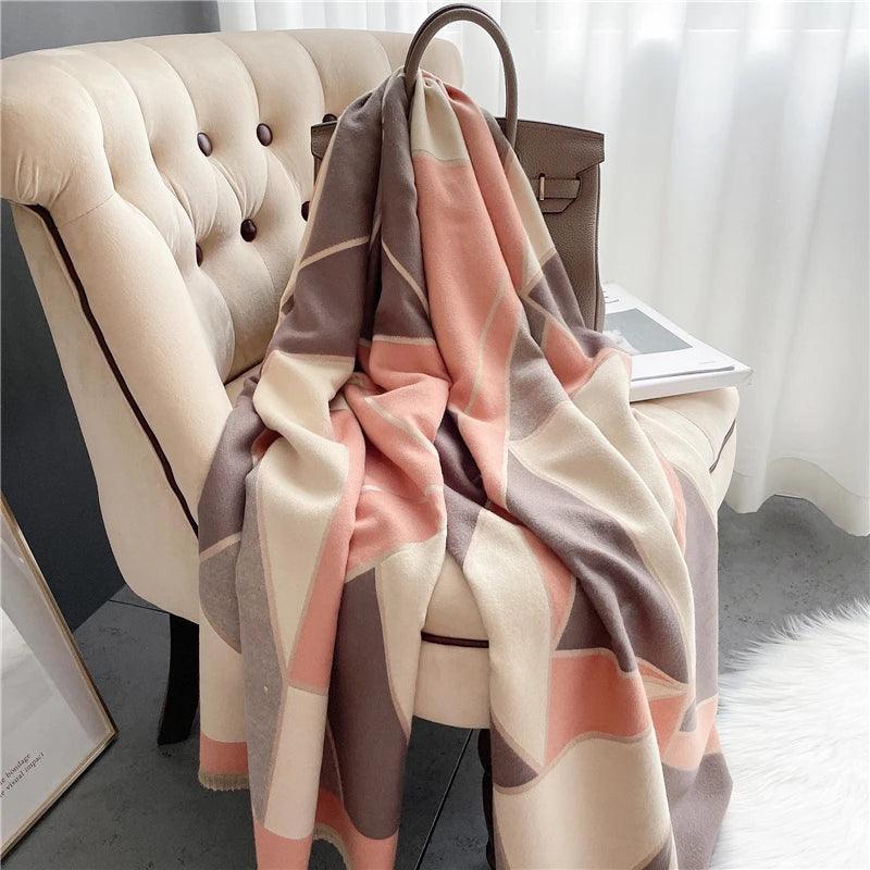 A cashmere scarf with geometric and floral patterns, draped over a chair with a handbag and a book on the arm of the chair.