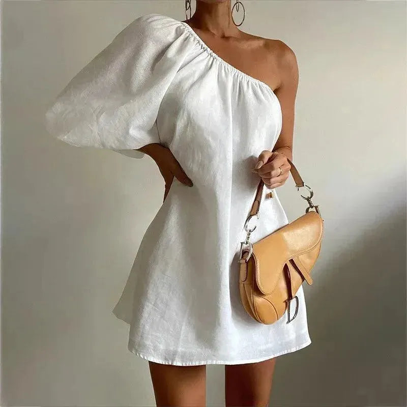 A woman wearing a white mini dress with a one-shoulder design and a brown belt bag.