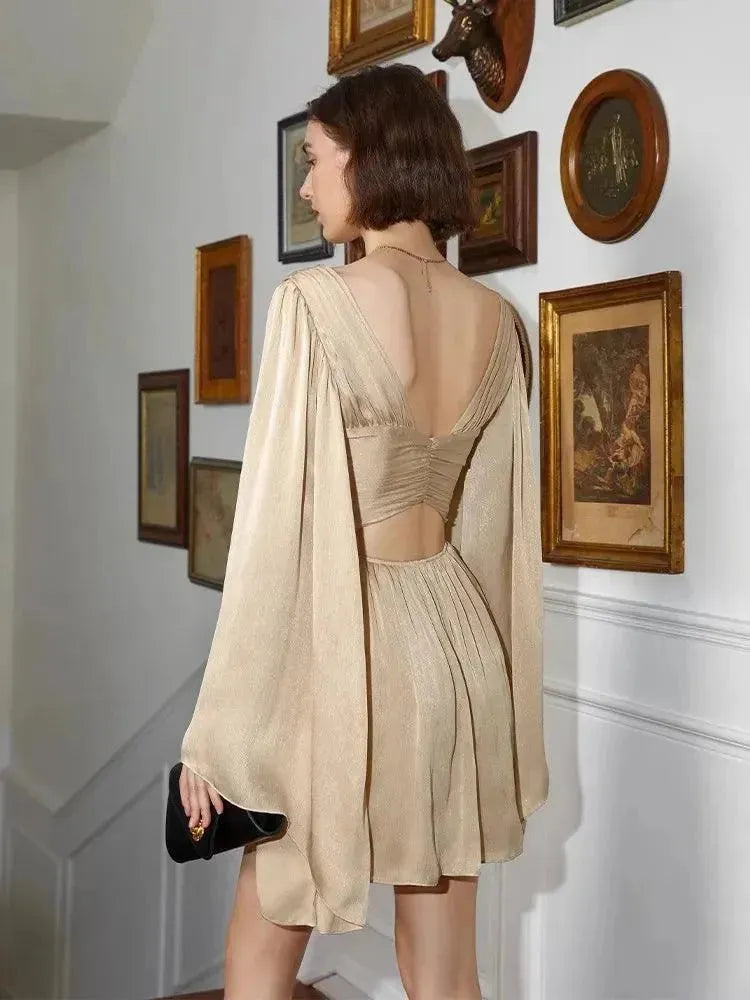 Woman in a beige dress with a black clutch in an room with framed pictures.