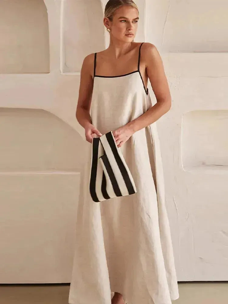 A model wearing a white maxi dress with black horizontal stripes, standing in a modern setting with a minimalist background.
