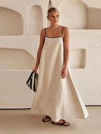 Woman in a white dress with black straps standing against a neutral background.