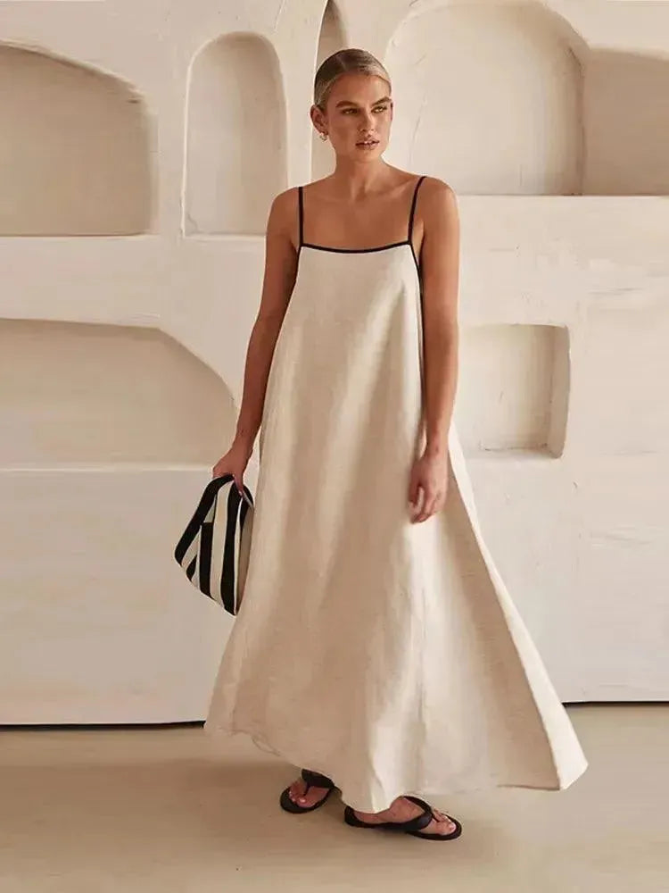 Woman in a white dress with black straps standing against a neutral background.