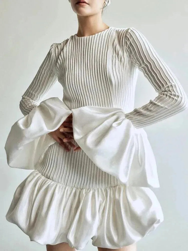 A woman wearing a white, floral mini dress with a V-neckline and long sleeves.