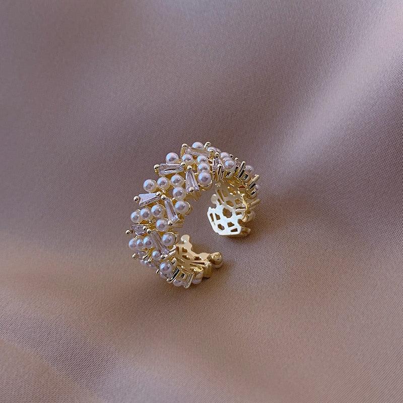 A gold-colored ring with simulated pearls set in a pave pattern, encircled by zircon accents on a textured background.